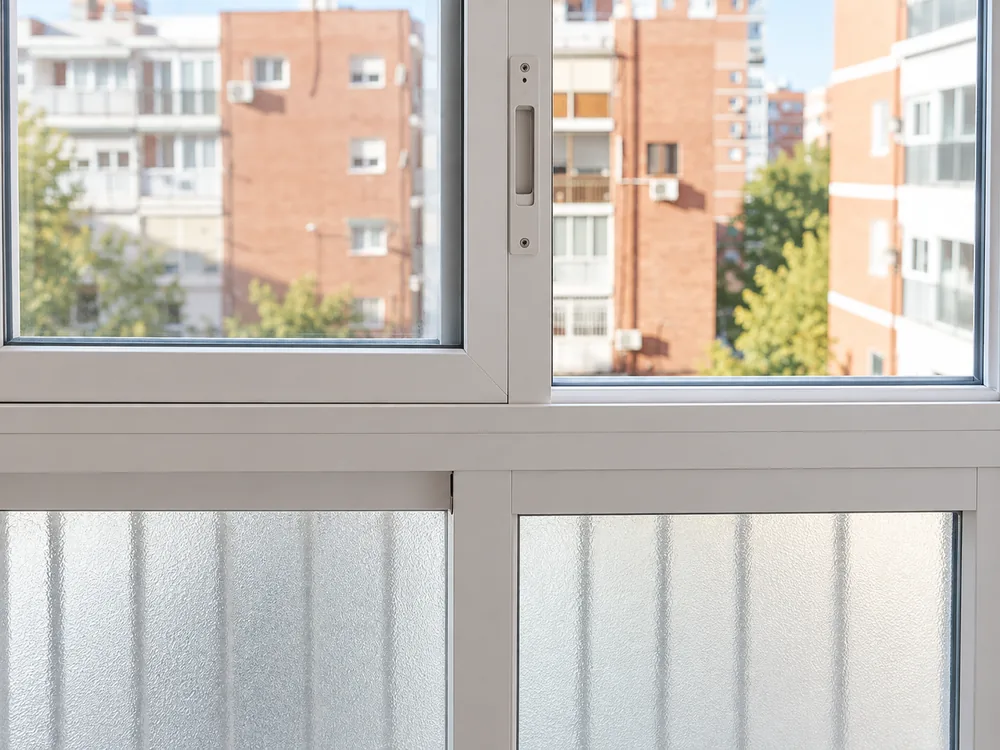 Detalle de cerramiento de aluminio blanco con hojas correderas y vidrio translúcido inferior