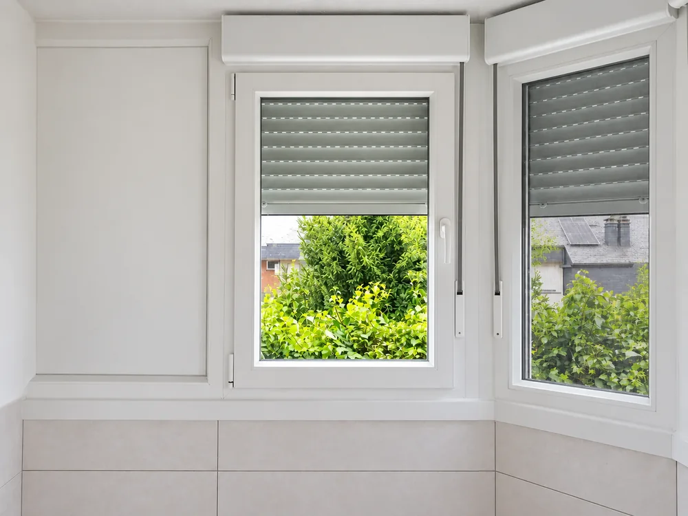 Ventanas de PVC blanco con persianas grises y mosquitera en la ventana derecha